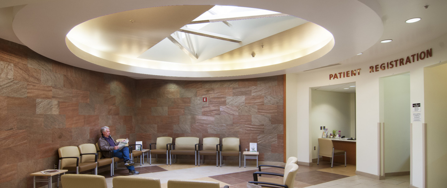 Reception in round room with tile wall and recessed geometric ceiling detail, white registration area and wood desk right