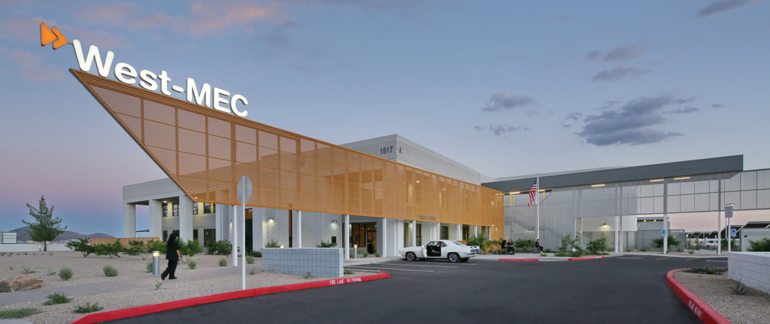 West-MEC Northeast Campus entrance with illuminated sign on top of orange perforated sunscreen extending past entrance