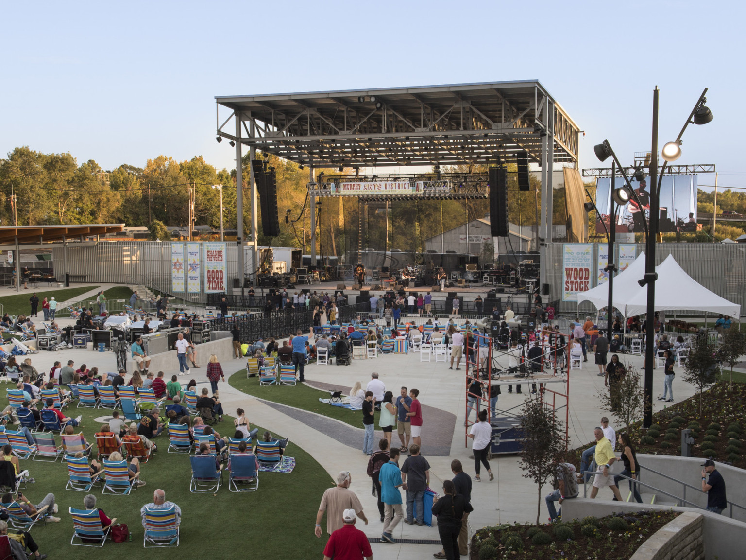 Crowd sitting in lawn chairs on grass and concrete facing outdoor stage