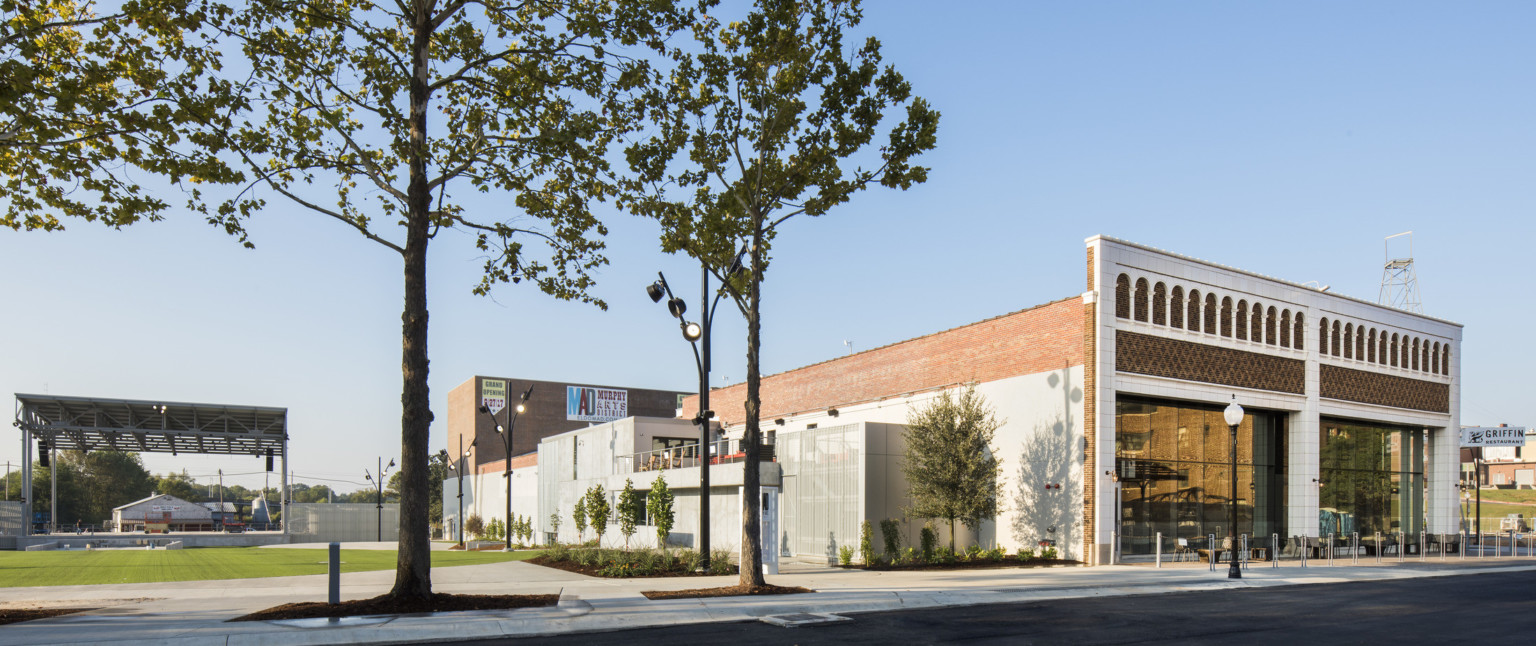 Corner view of brick building with white molded facade next to green field with pavilion roof