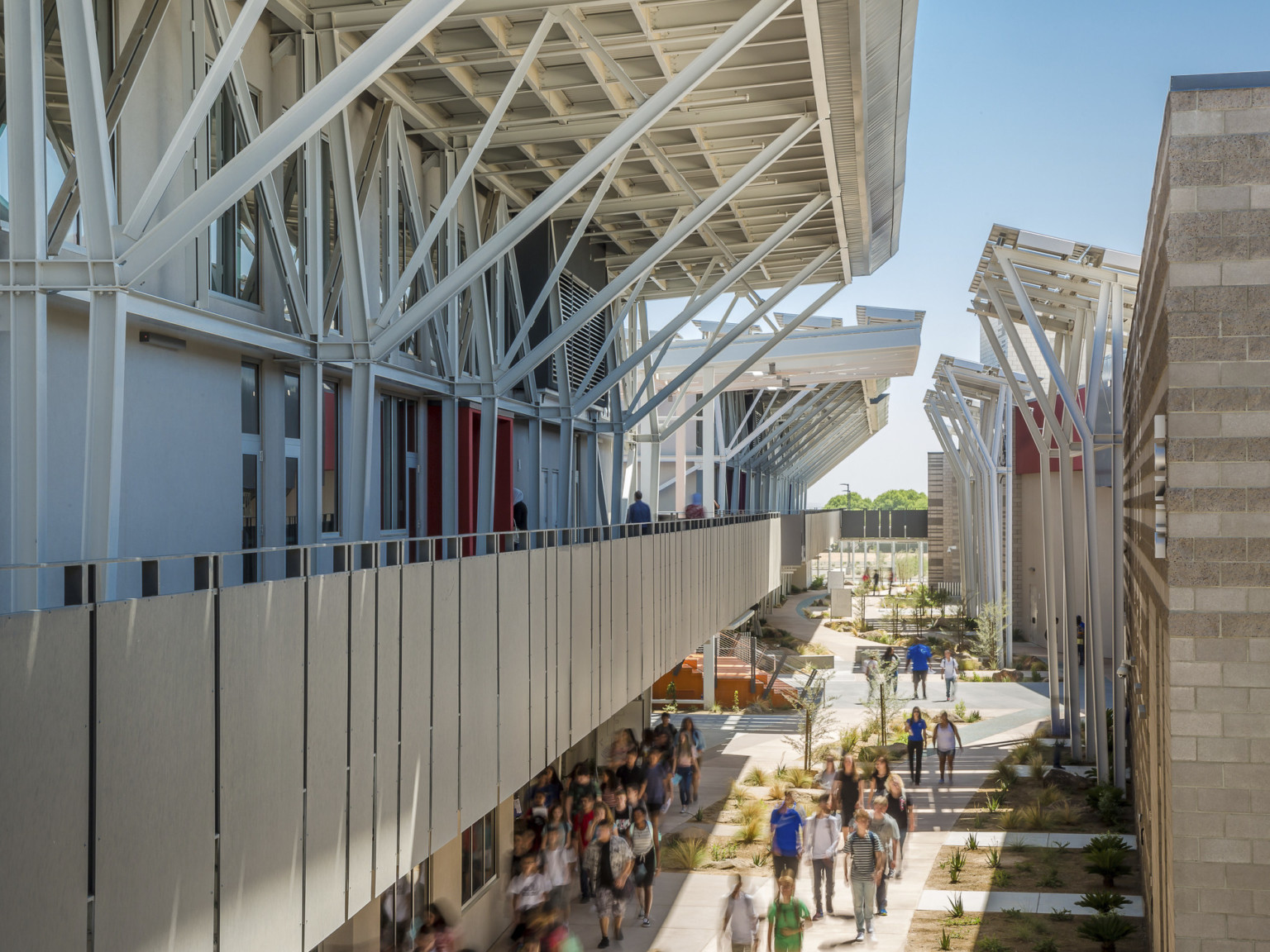 Second floor partially covered exterior walkway extends over paths with greenery between buildings, framed by exposed beams