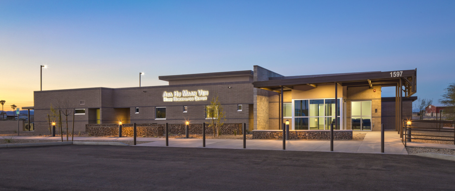 Front of building illuminated from recessed lights in overhang. Lit sign left reads Ava Hu Maan Veh Home Hemodialysis Center