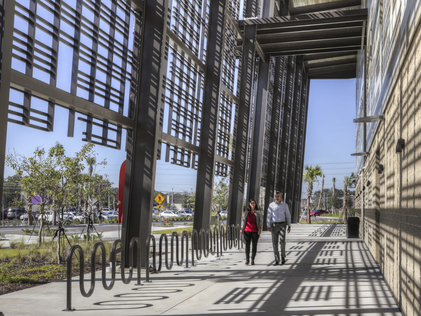 Walkway along perimeter of building. Bike racks right below geometric wrap on upper levels of building creating shadow design