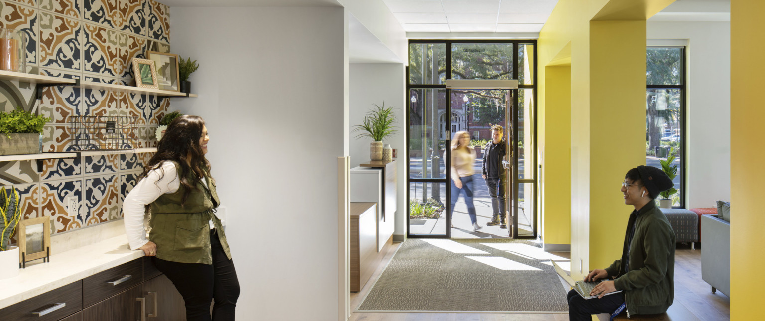 Hallway left of yellow wall to entry. White room towards the door behind recessed dark wood counter with muraled backsplash