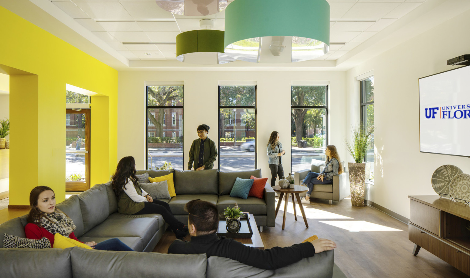 Side view of room, yellow accent wall left of white walls with floor to ceiling window sections. Colorful light shades above