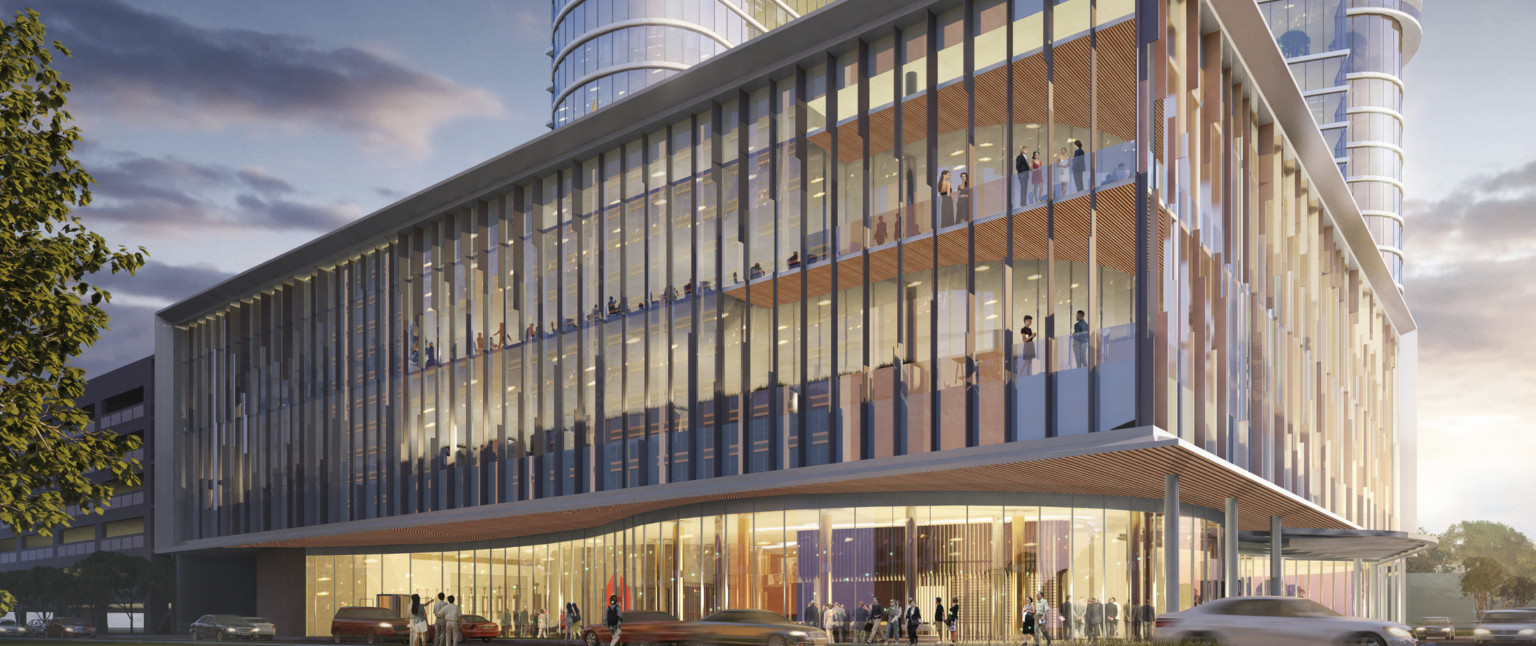 Lower building seen from corner, illuminated at night. Upper levels extend over curved 1st floor lobby. Building tower behind