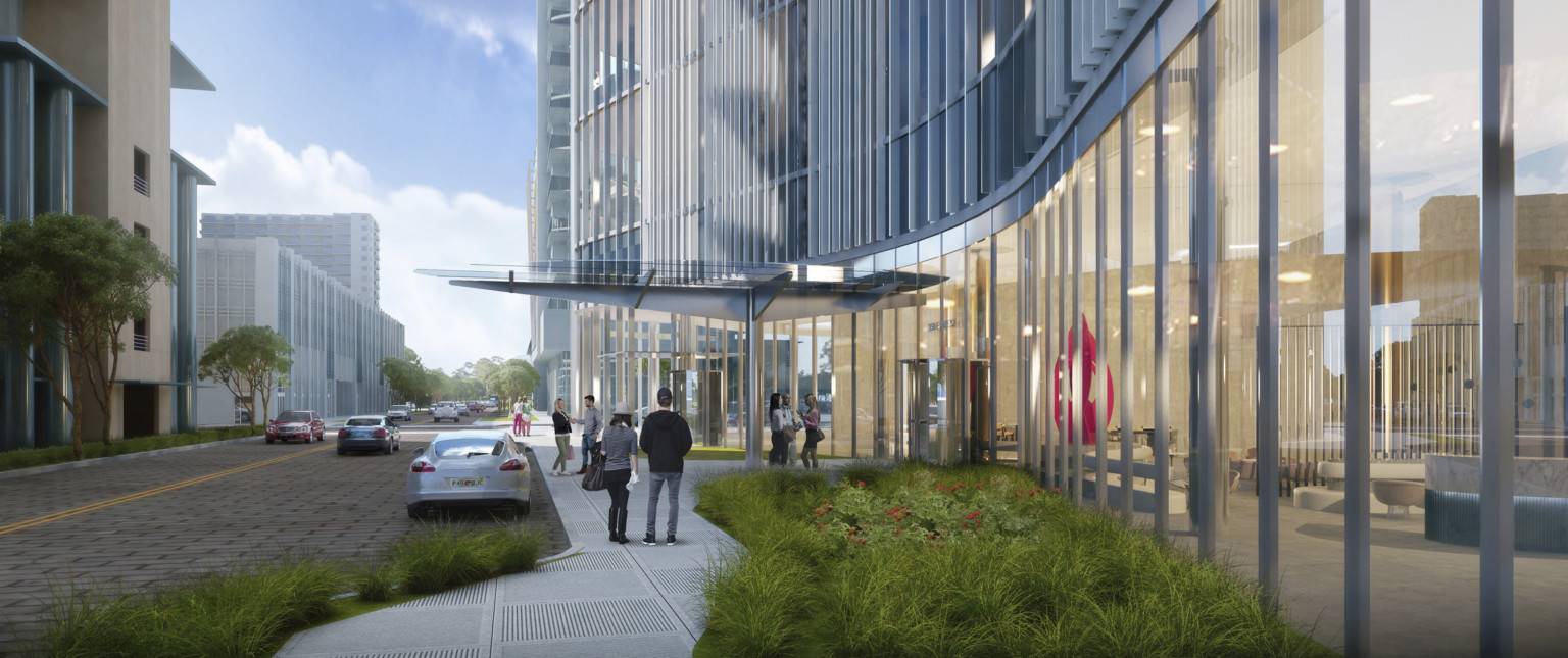 Building entry with glass shelter supported by metallic pillar and trusses leading to revolving door to lobby