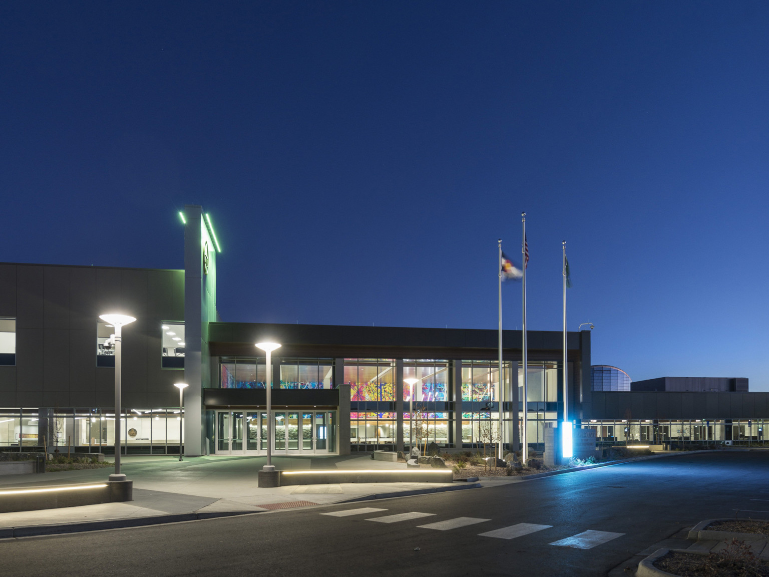 Building entry at night from across the street. Upper wall lit in green from above, with blue glow at building's lower right