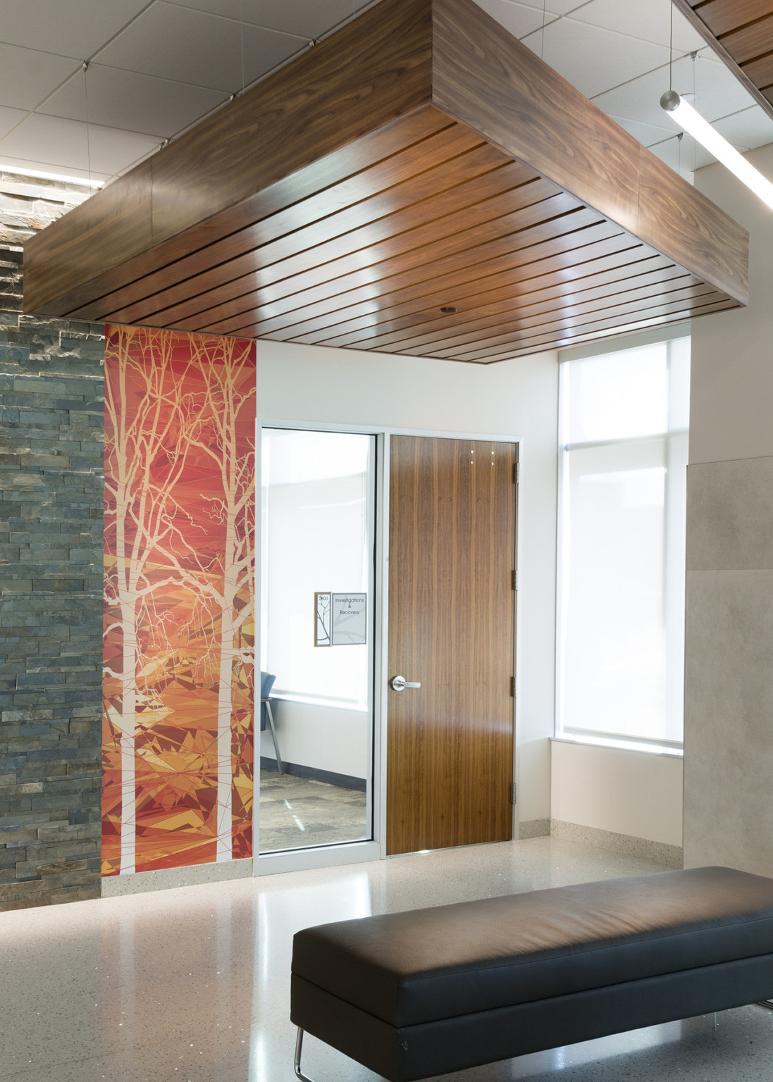 Wood paneled box hangs from ceiling next to light fixture above door. Orange wall mural is between door and stone wall detail