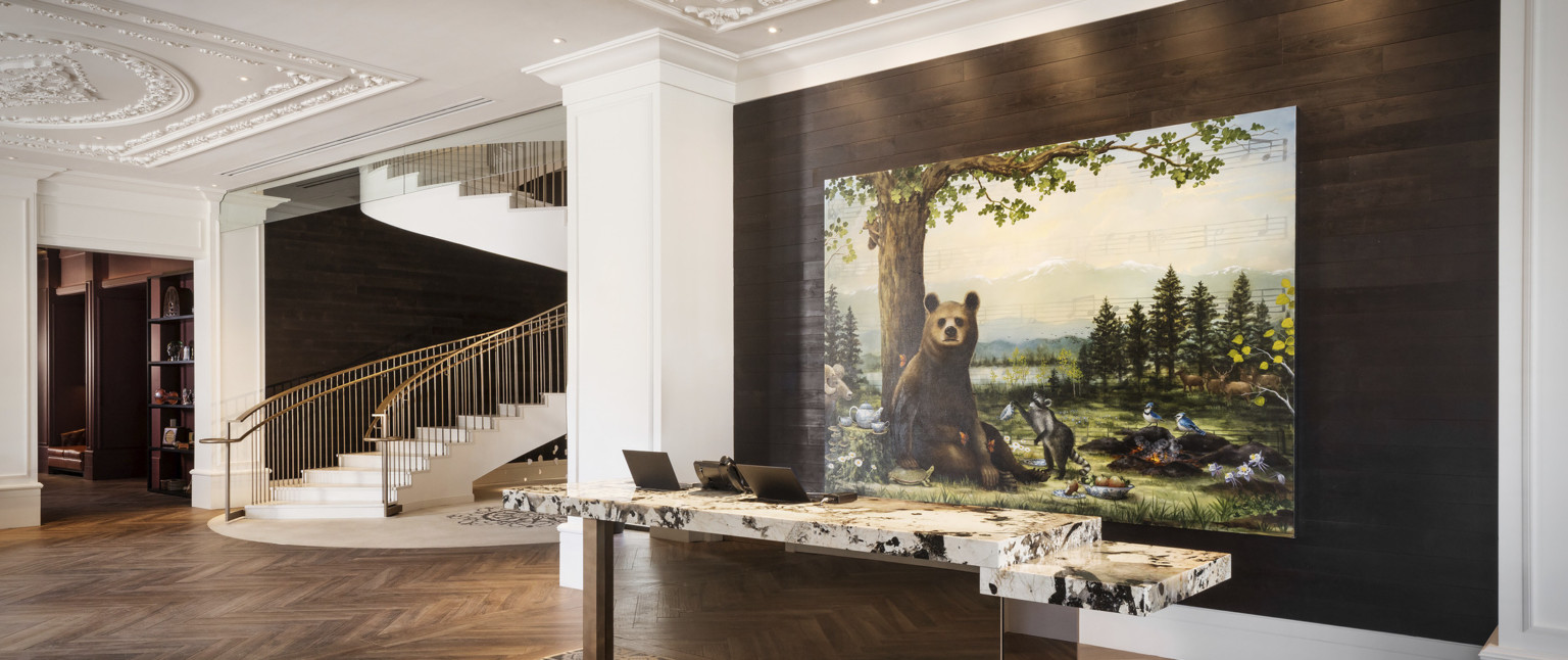 Reception desk with white and black marble counter in white lobby in front of recessed wood wall with painting of a bear