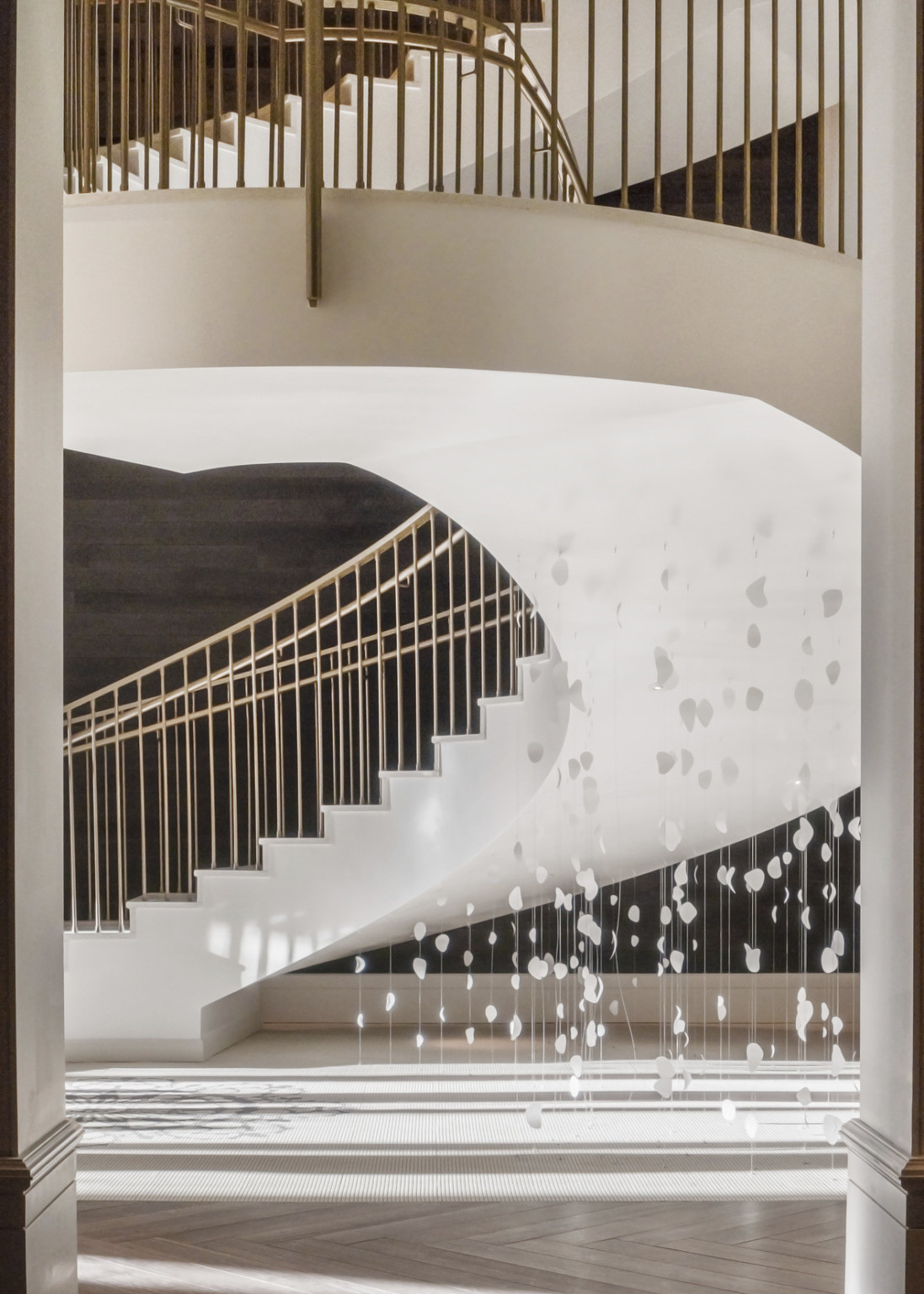 Closeup of spiral staircase from ground level framed by a doorframe. Strung white shapes hang from beneath the stairs