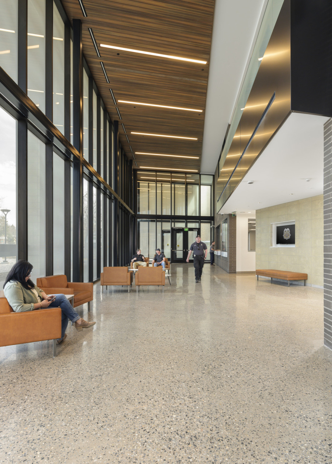 Entry hall of large windows with dark frames and seating areas with orange armchairs under wood panel ceiling with lighting