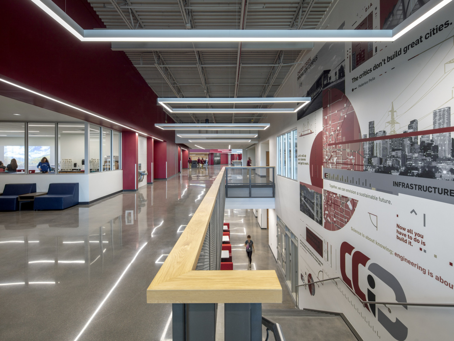 Mural on right wall next to stairs to 2nd floor. Red wall to left with white recession with seating by classroom windows