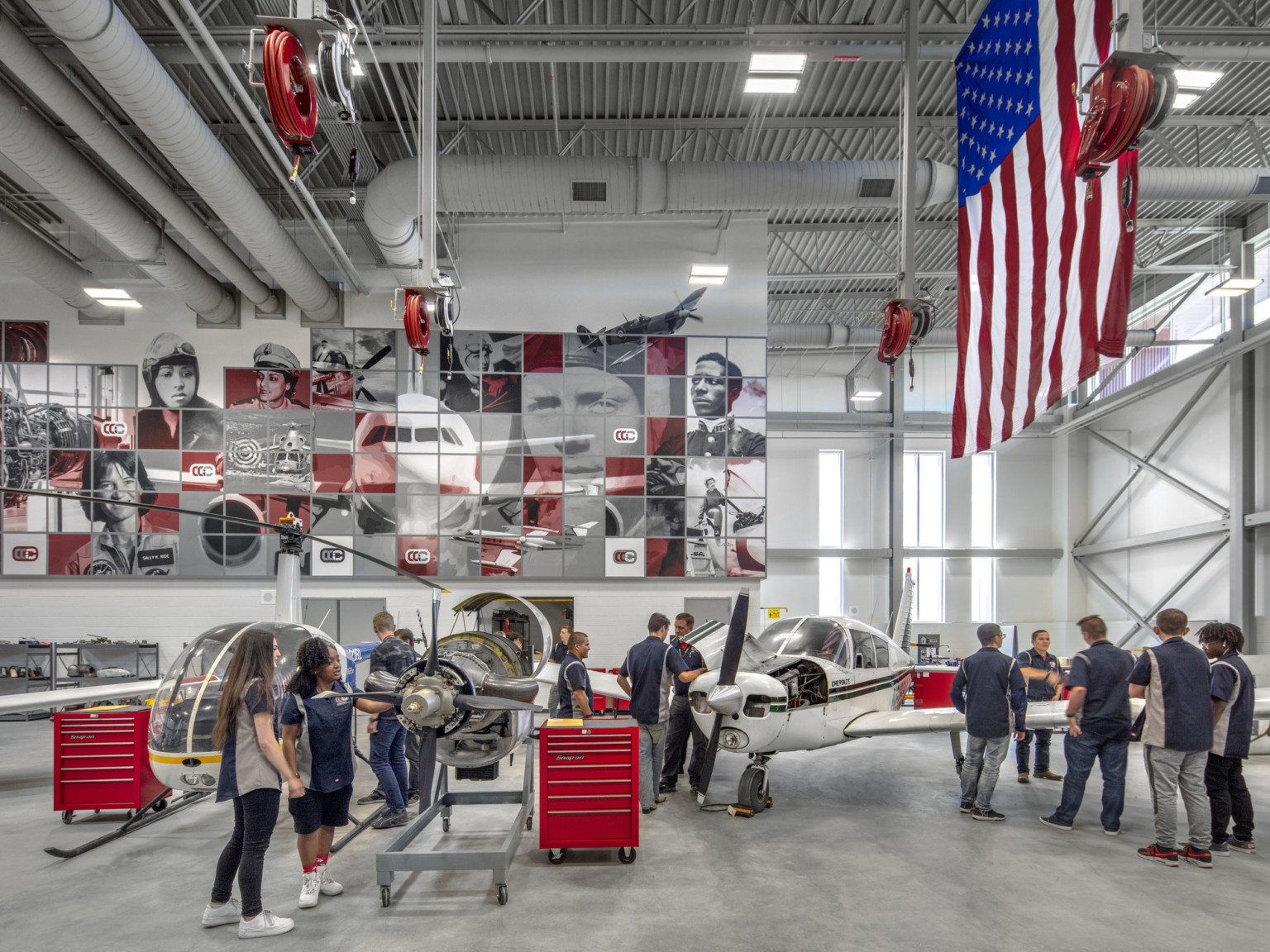 Aviation lab with helicopter, small plane, and displayed engine. Mural at back with planes and pilots. American flag, right