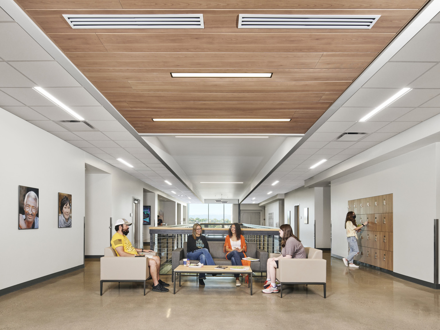 Atrium in hallway past reception with elevators to right in grey wall, walkway with grey bannister above