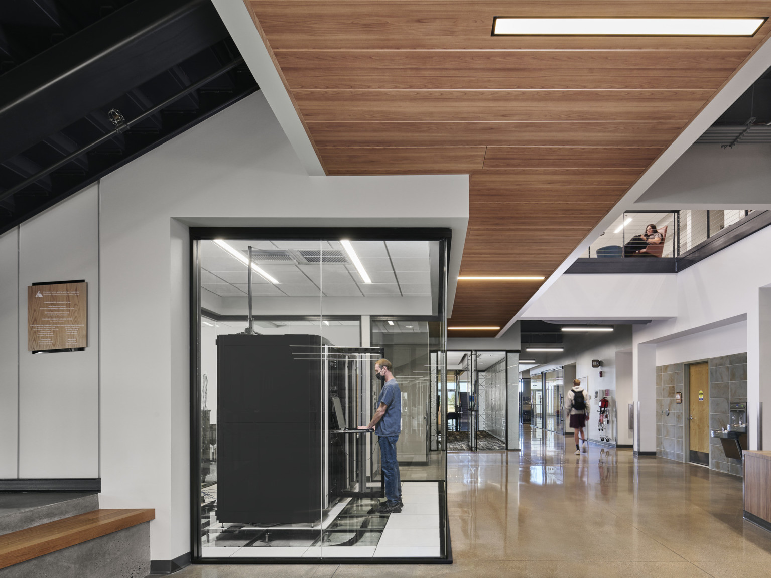 Private work areas with glass walls in space below upper walkway. Translucent wall and door with geometric design