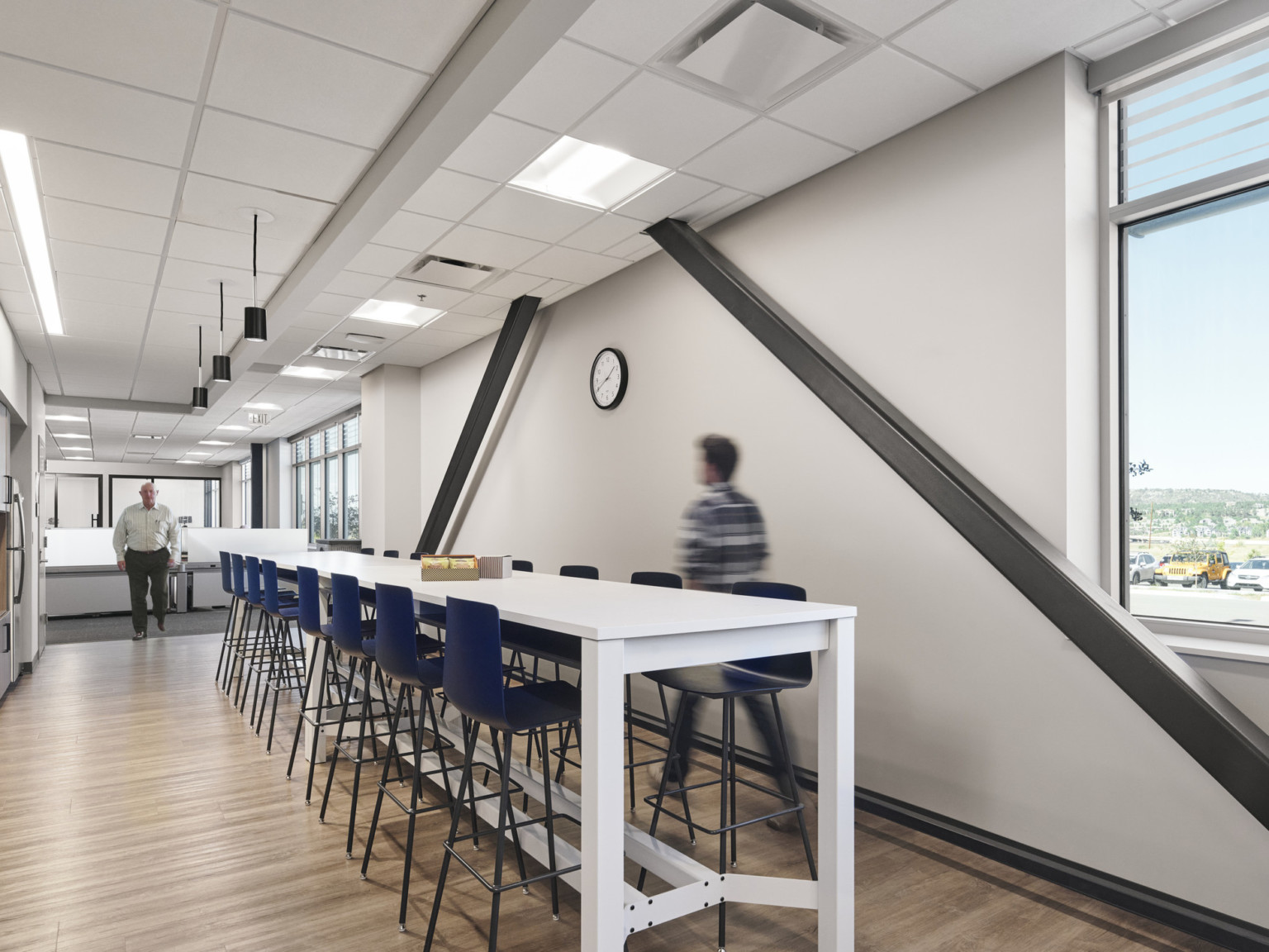 White hallway with angled black exposed beams, right, and white island table along center with blue stools