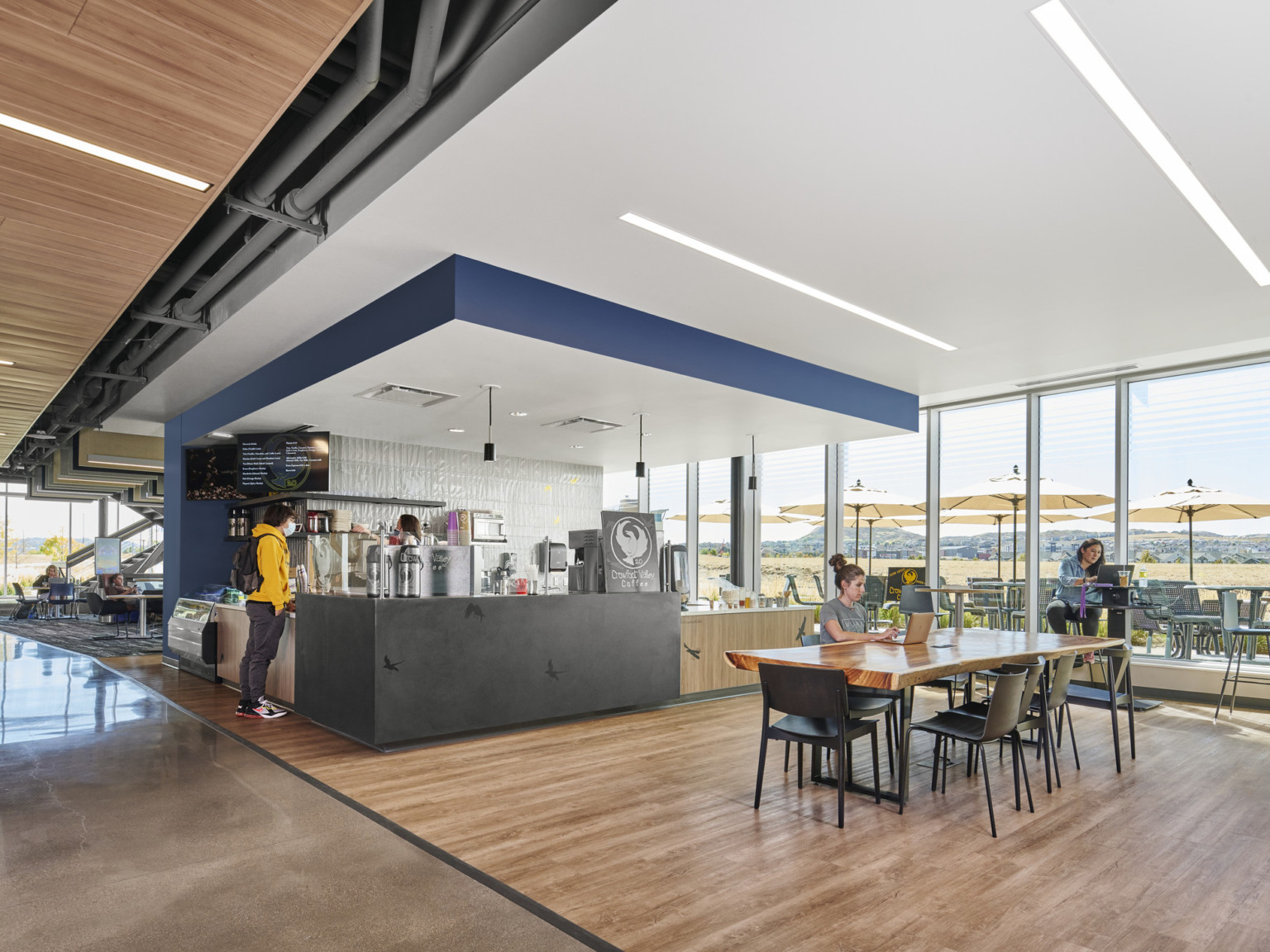 Small dining area off hallway with counter under drop ceiling detail with blue accent. Hard wood flooring and large windows