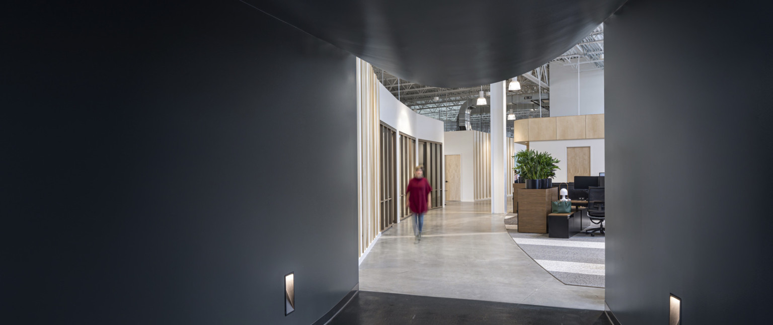 View from black hallway looking towards double height room with exposed beams and white walls with wood accents