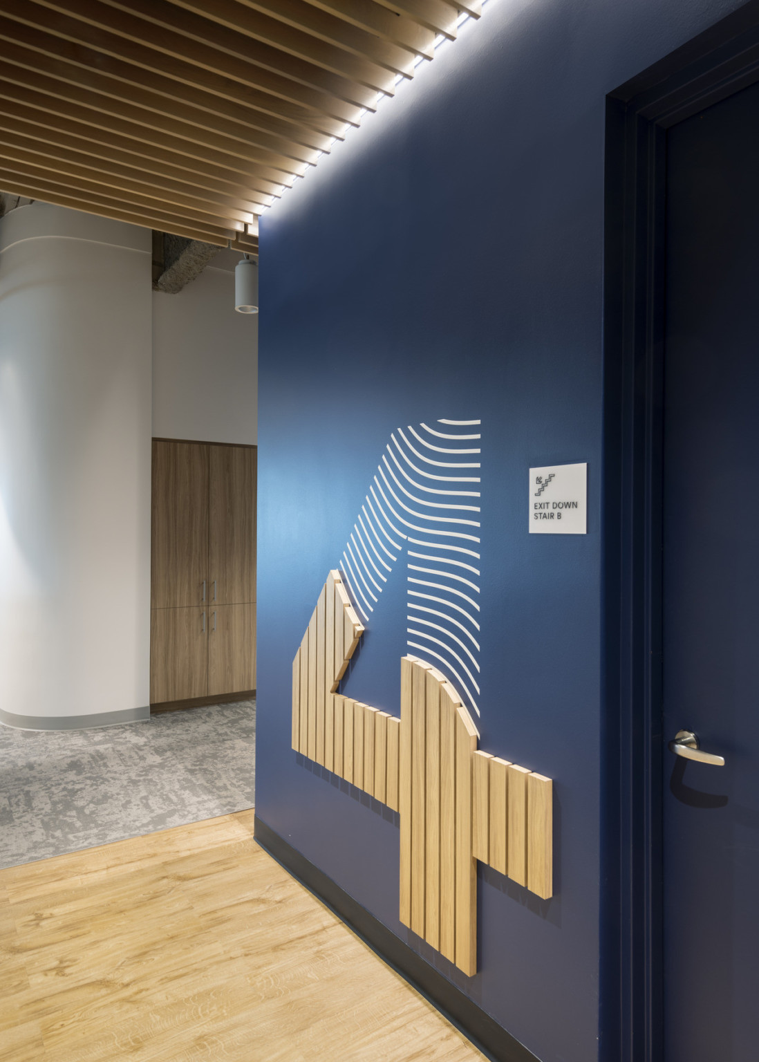 Wood slat ceiling above dark blue wall with large number 4 with 3 dimensional base off of white hallway