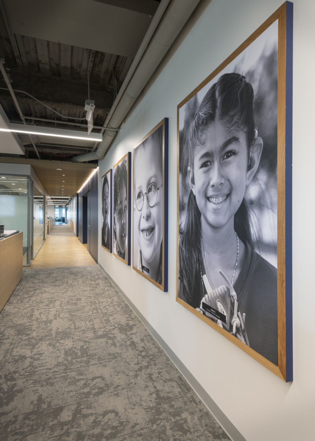 Black and white portraits of children in light wood frame hang on white wall to right in hallway