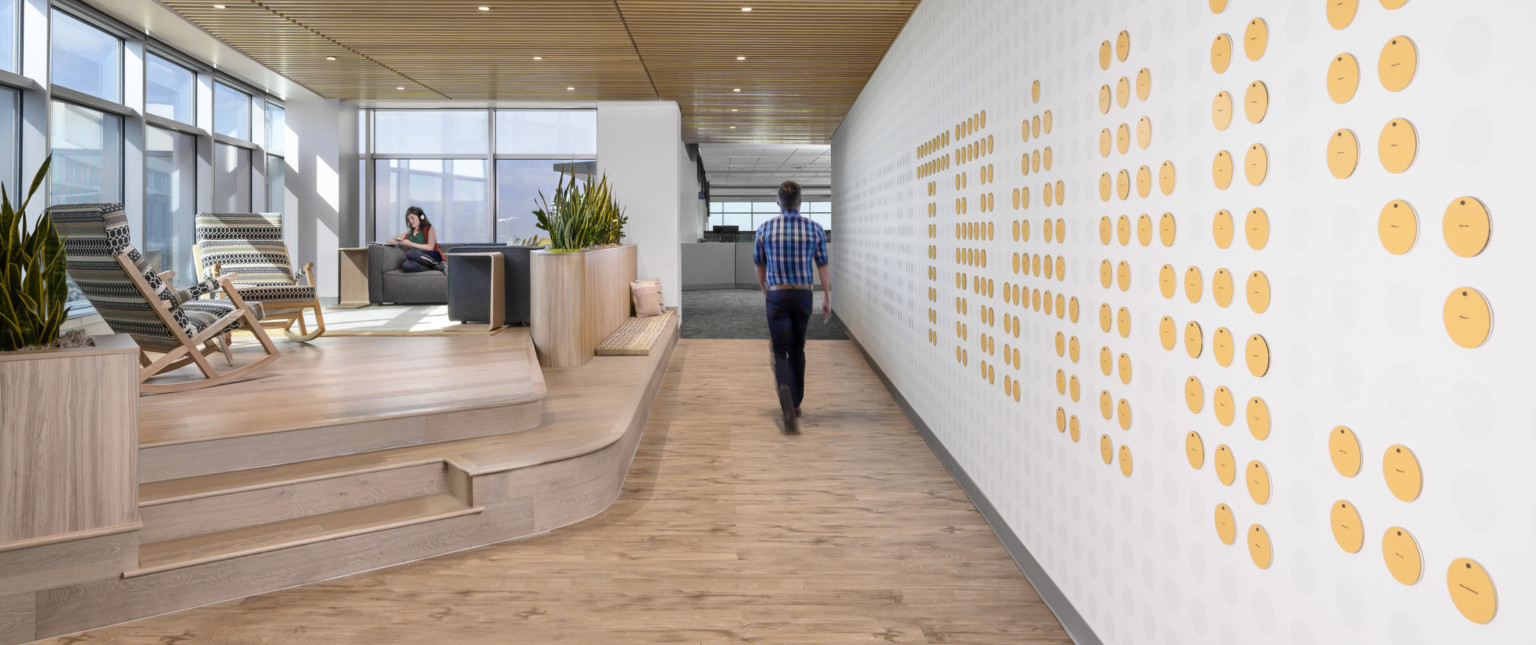 Wood slat ceiling over hallway, mezzanine with floor to ceiling windows and seating to left. Wall, right, with circle details