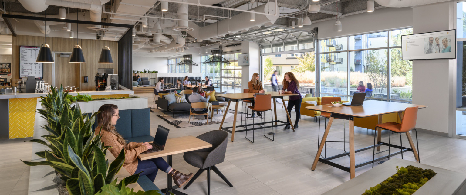 Mixed seating with tables in room with floor to ceiling windows with open garage style door, right. Coffee counter to left