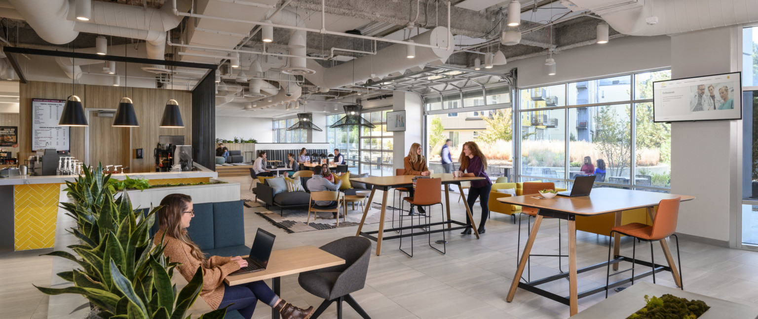 Mixed seating with tables in room with floor to ceiling windows with open garage style door, right. Coffee counter to left