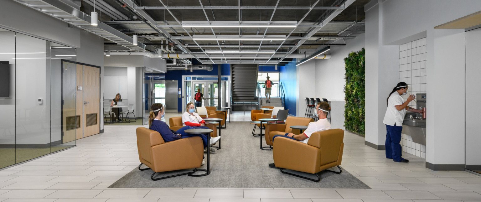 Seating area in entry with individual orange arm chairs with round tables over carpet section. Blue stairwell by doors