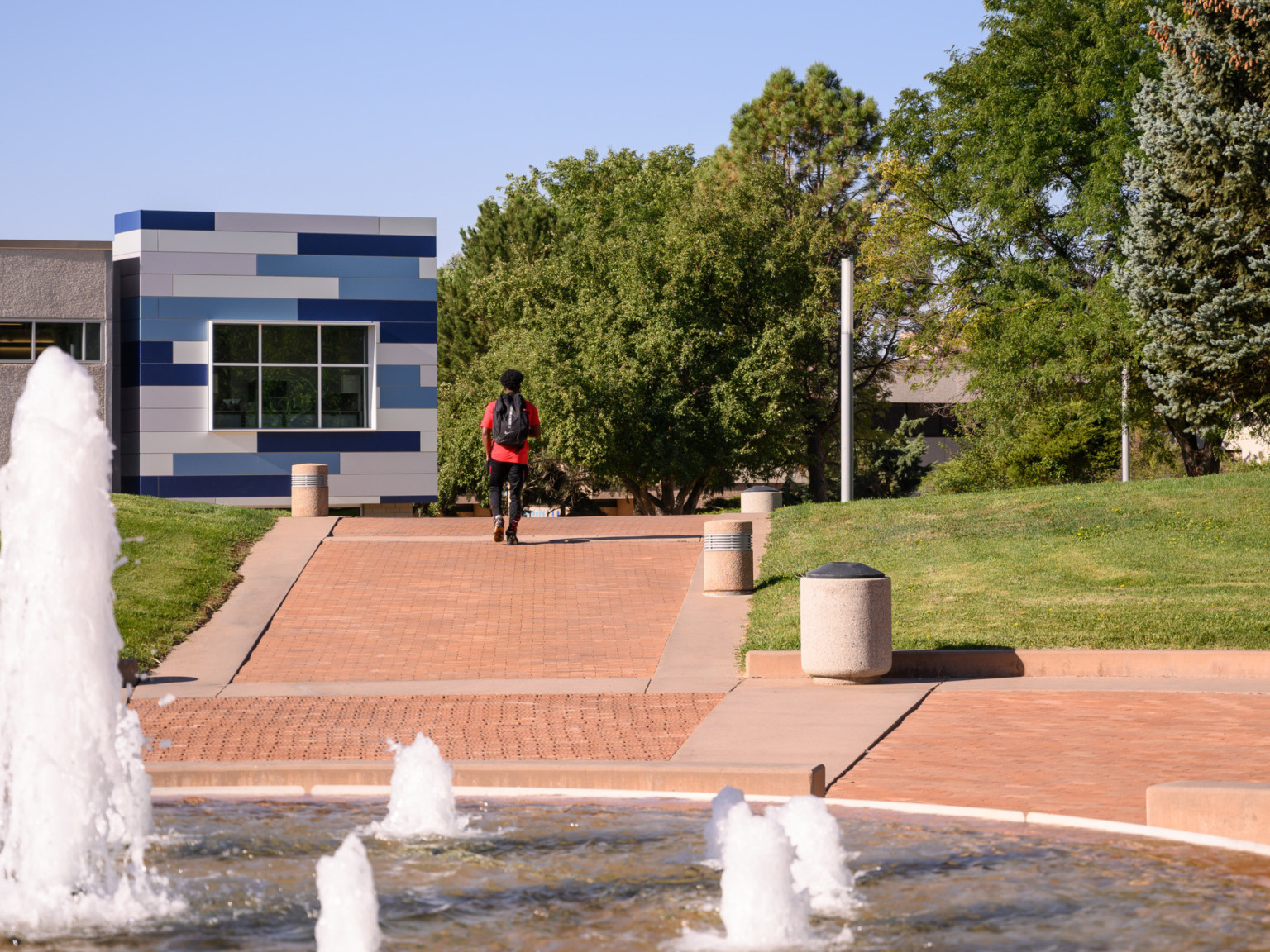 Fountain in center of rounded walkway with path leading away in tree lined greenspace outside of building