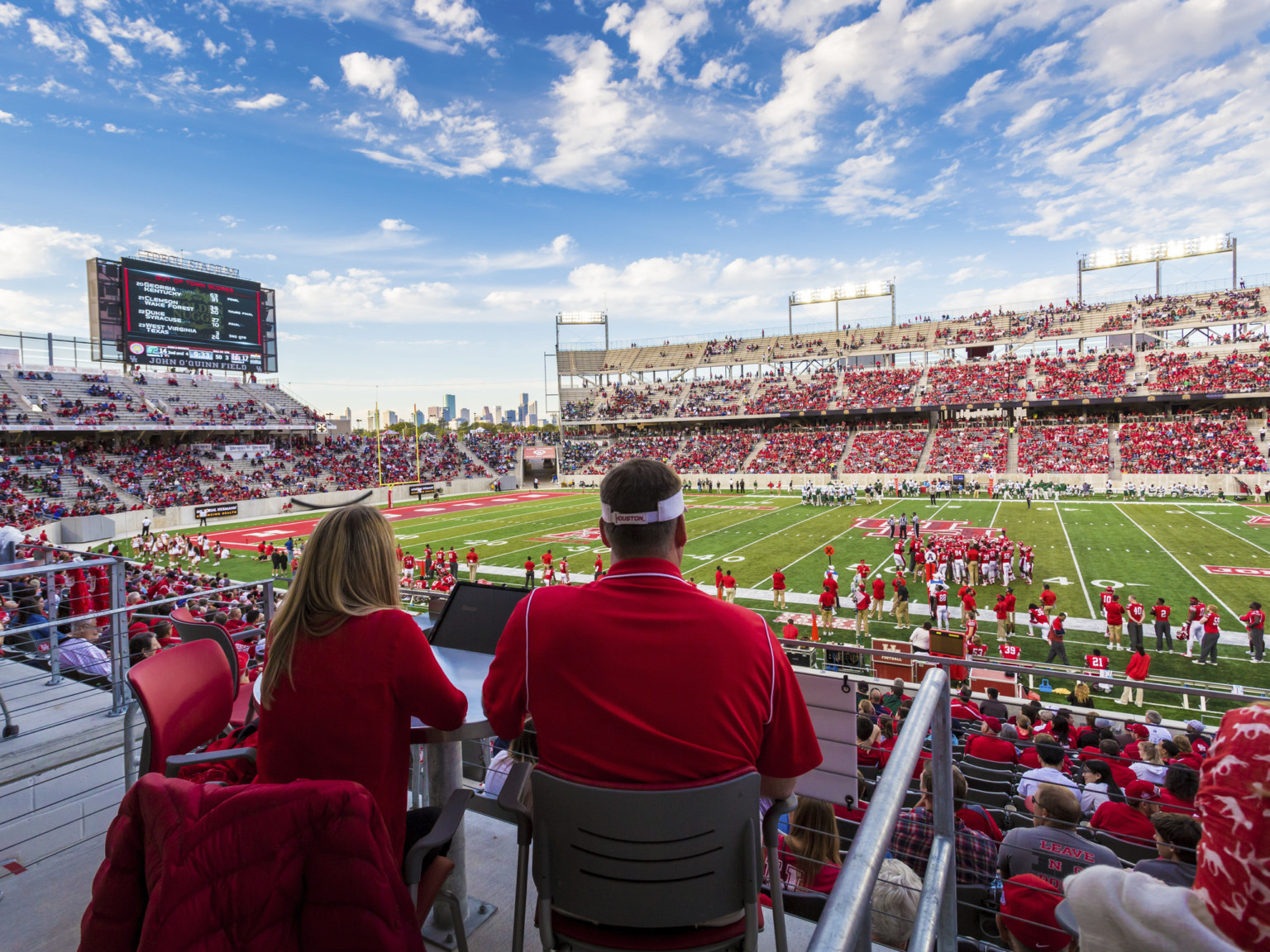 Flexible seating in outdoor boxes on midlevel, looking to field on game day. Jumbotron above seats behind end zone