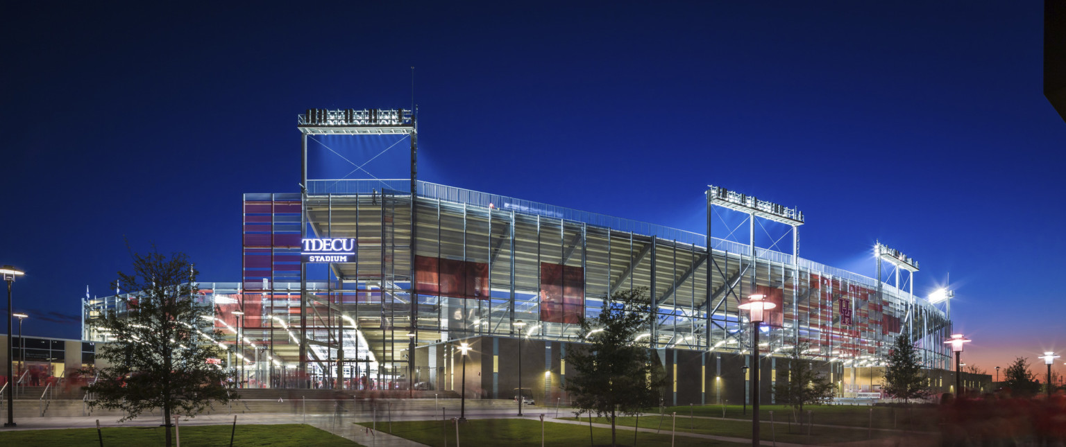 Side view of structure with TDECU Stadium sign illuminated. View through sunscreen to illuminated beams and back of bleachers