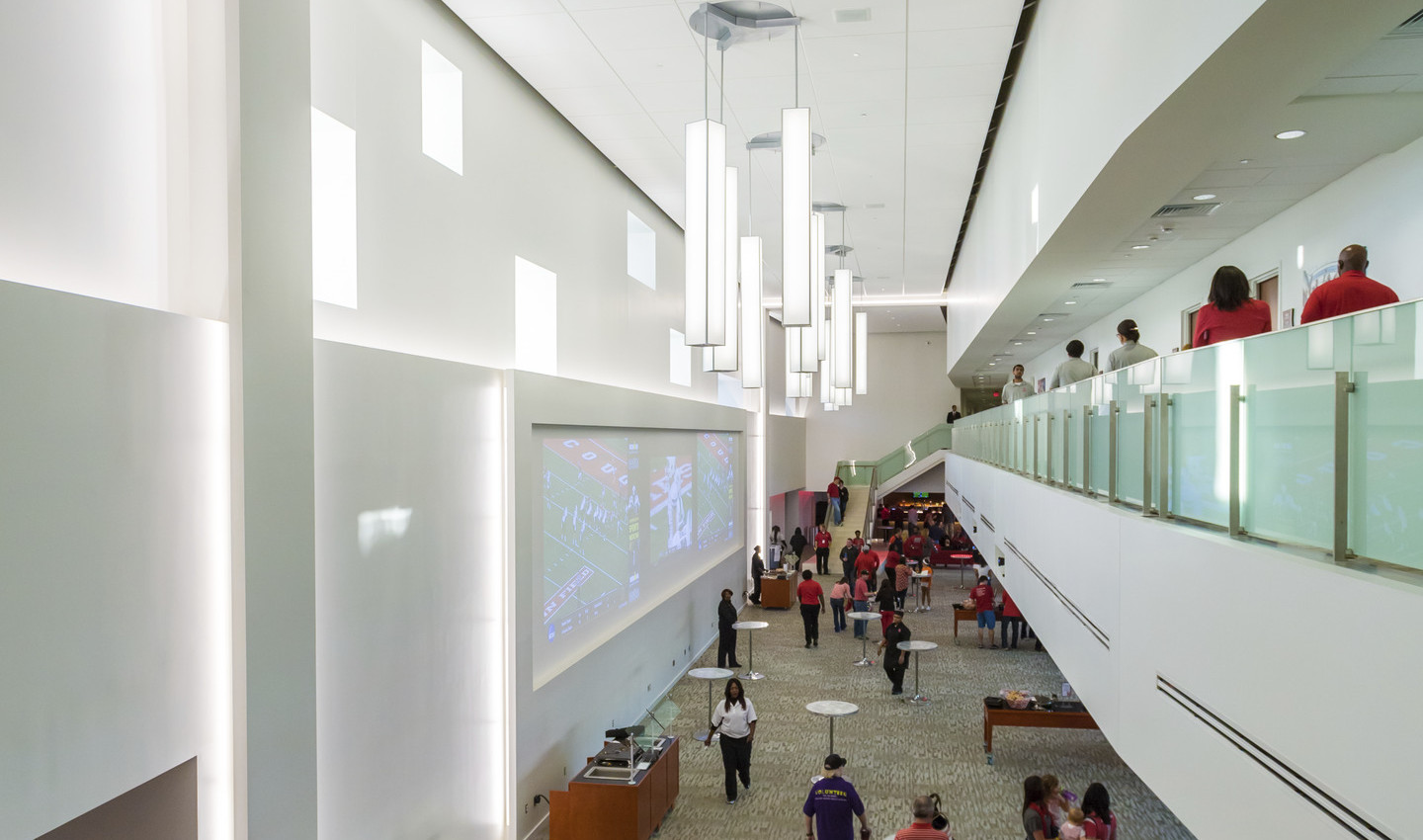 Interior double height room with tables on 1st floor, 2nd floor walkway with glass rail, right. Sculptural chandeliers hang