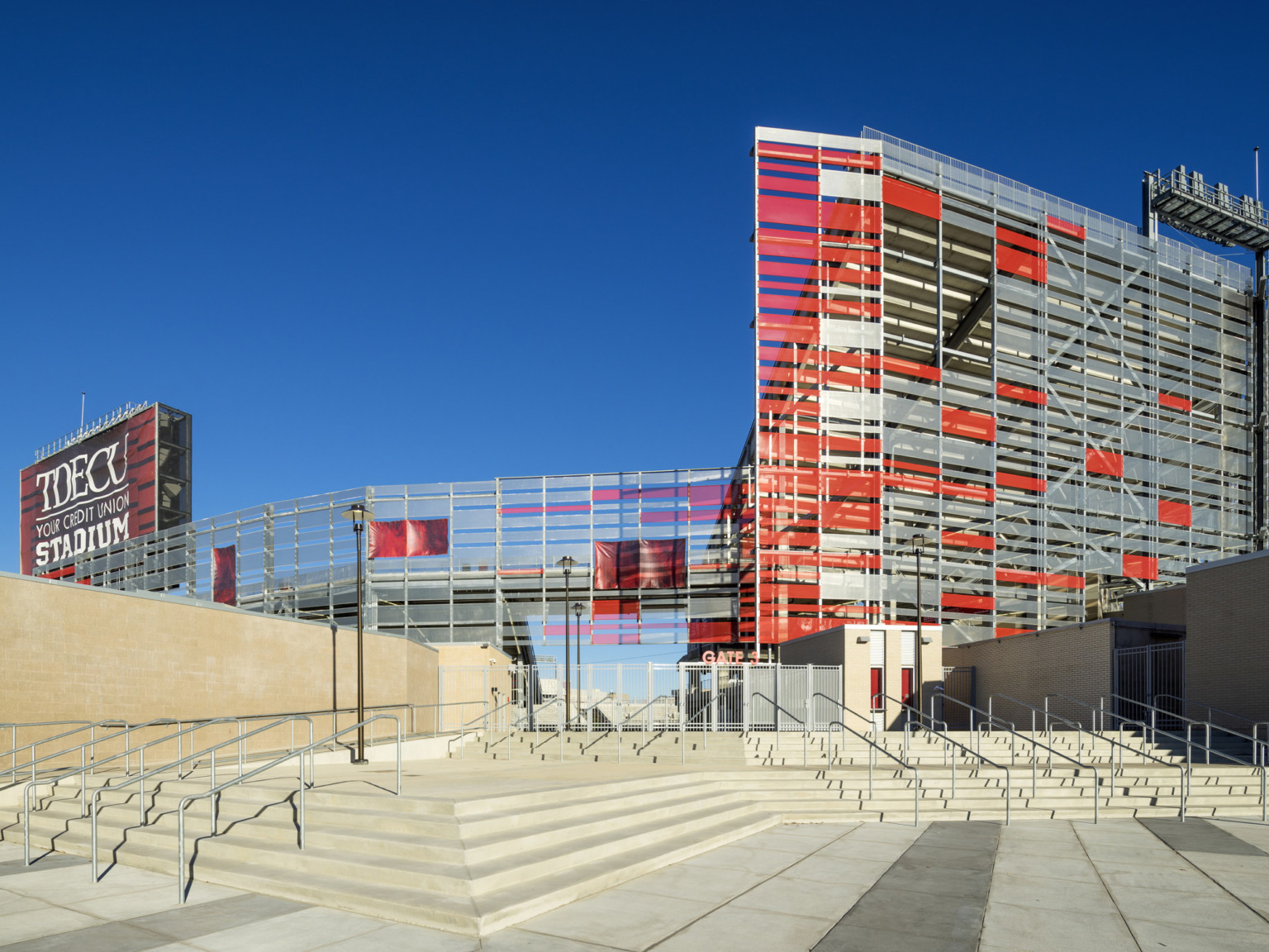 Stone steps come from different angles to stadium entrance framed by buildings. TDECU Stadium banner on left of sunscreen