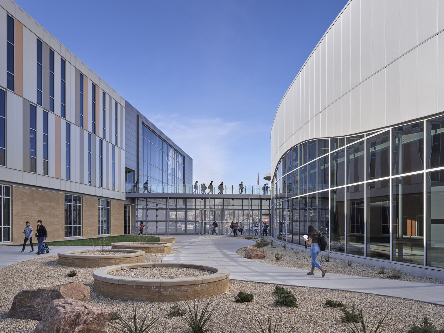 Courtyard with curving paths and round planters in stone garden. Front, a double height window hall connects the 2 building