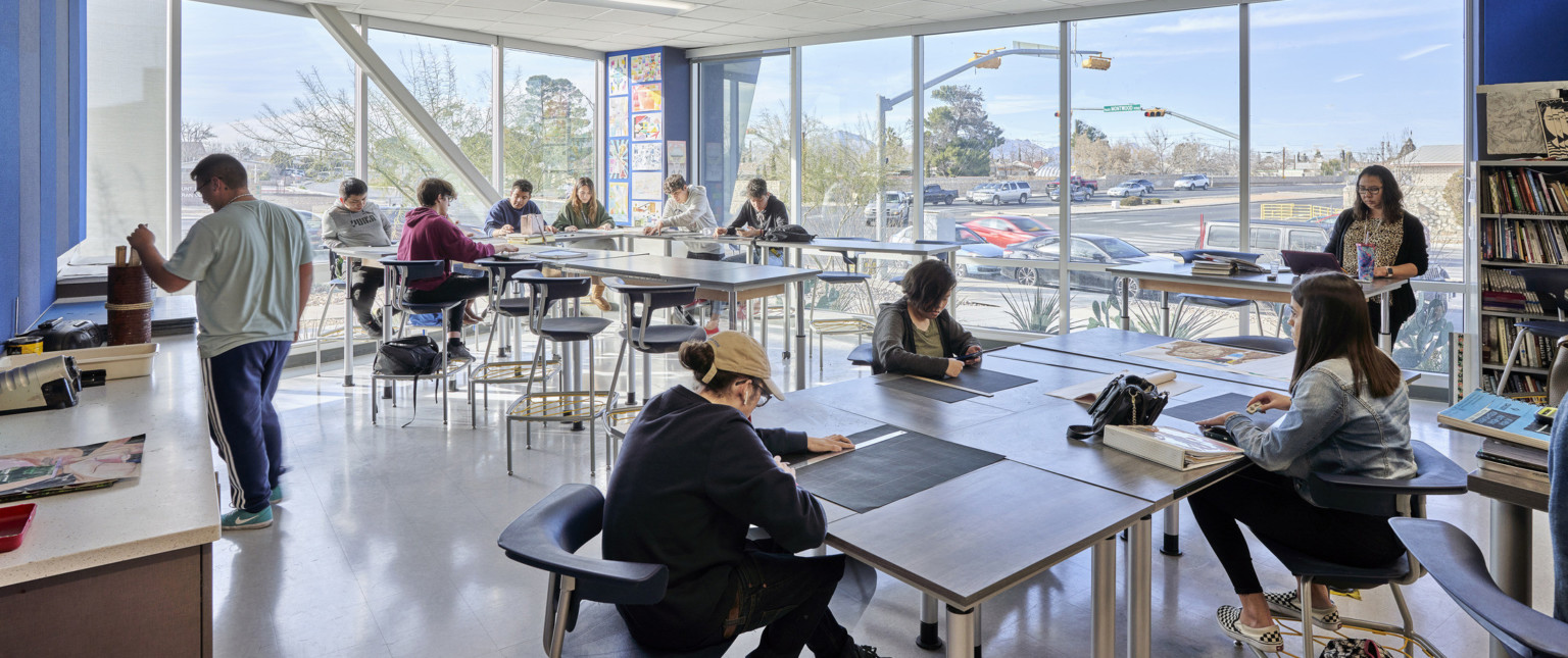 Corner art room with floor to ceiling windows looking out to street. Tables of varying heights in a room with blue walls