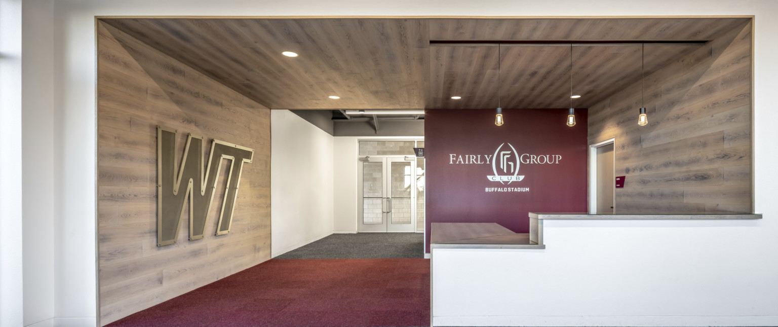 Wood panel room with WT logo on left and red accent wall on right at back with Fairly Group Club logo. Pendant lights above