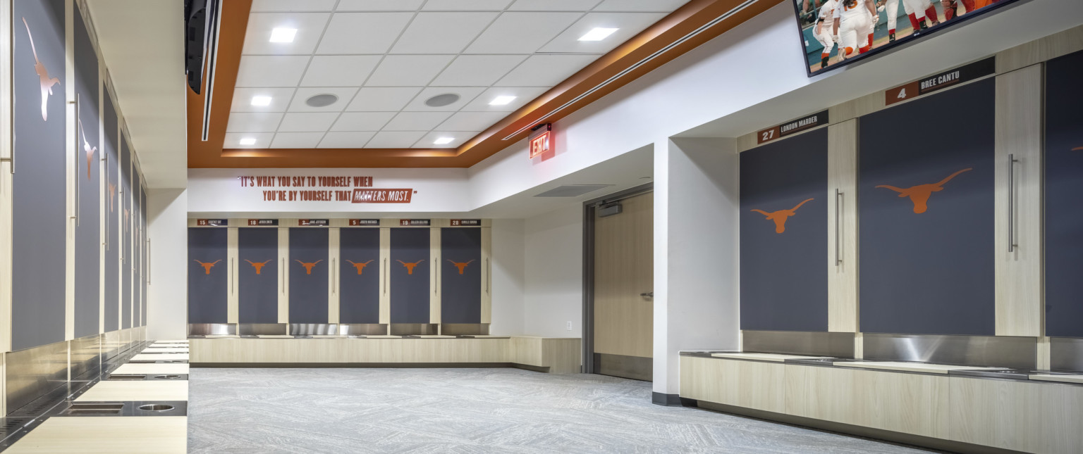 Locker room with orange logo on recessed grey lockers. White room with recessed ceiling framed by orange border