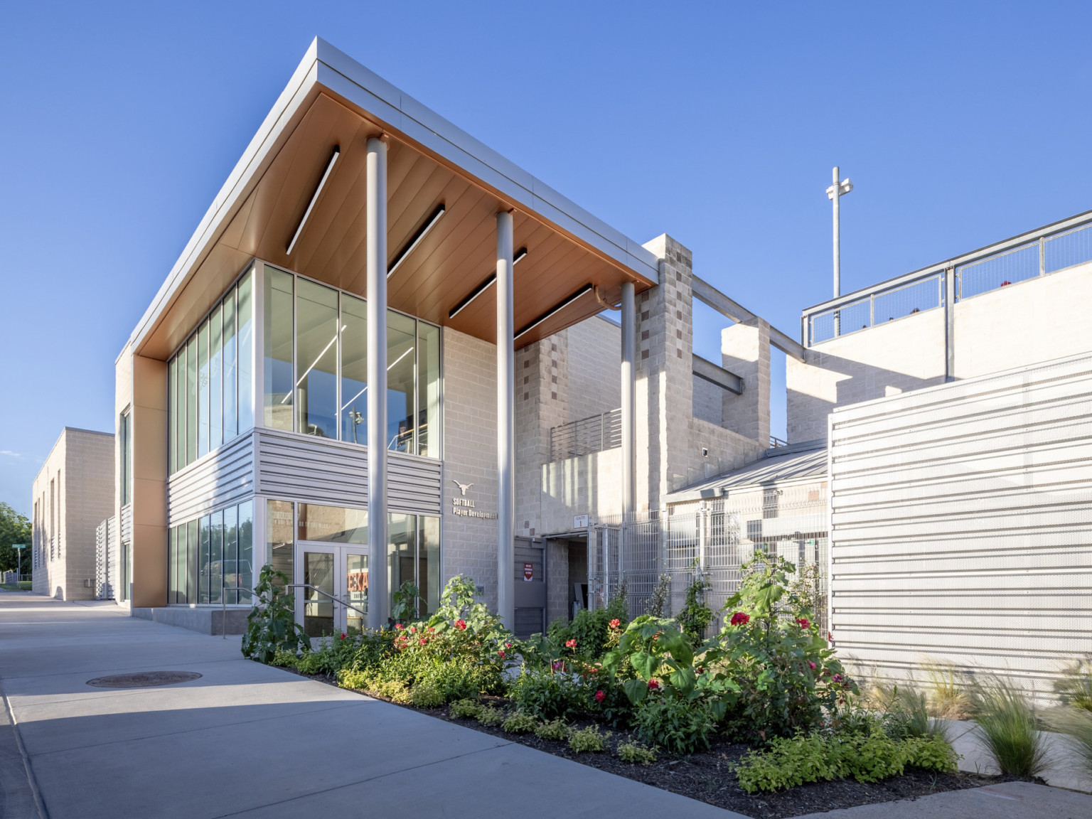 Corner view of white panel building with glass front and partial side. Wood base on canopy wrapped facade with white columns