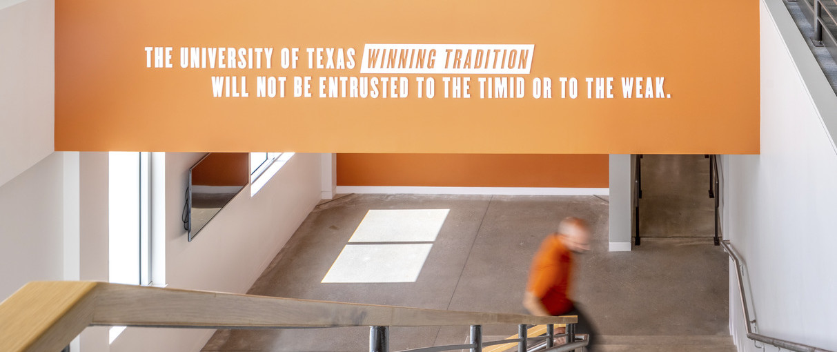 Stairwell below orange mural reading The University of Texas winning tradition will not be entrusted to the timid or the weak