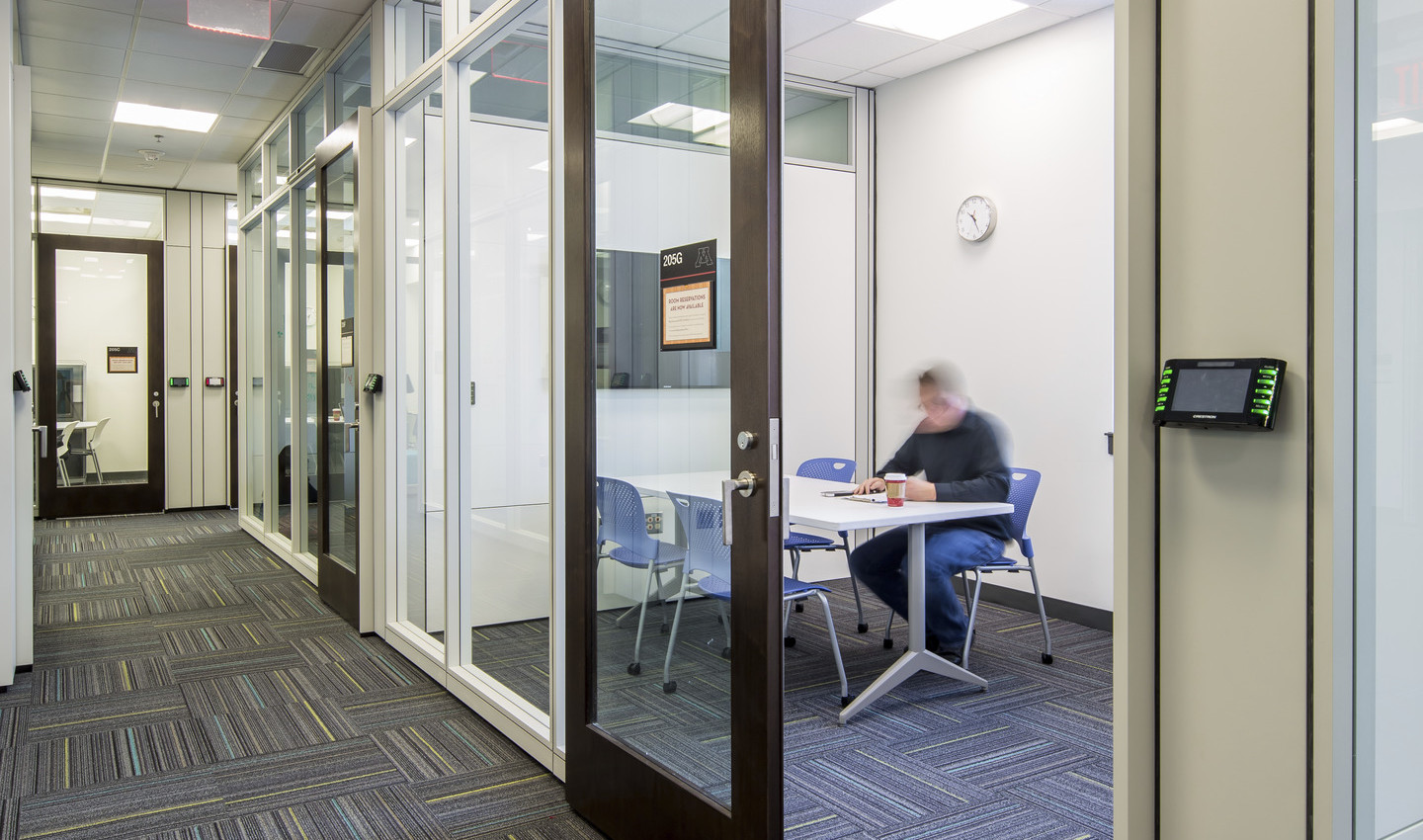 man working in a private room with glass walls and door off a hallway in the University of Minnesota Student Cultural Center