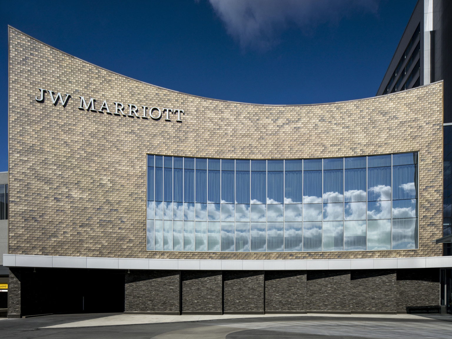 Closeup of curved brick lower building with JW Marriott sign and panel of double height windows above garage entrance