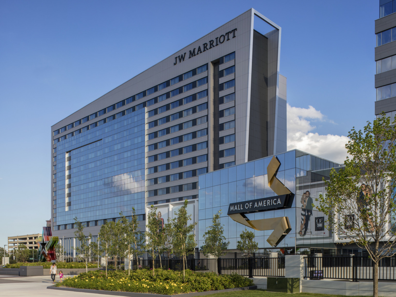 Hotel seen from sidewalk with glass building right. Blue and yellow ribbon shaped sign on building reads Mall of America