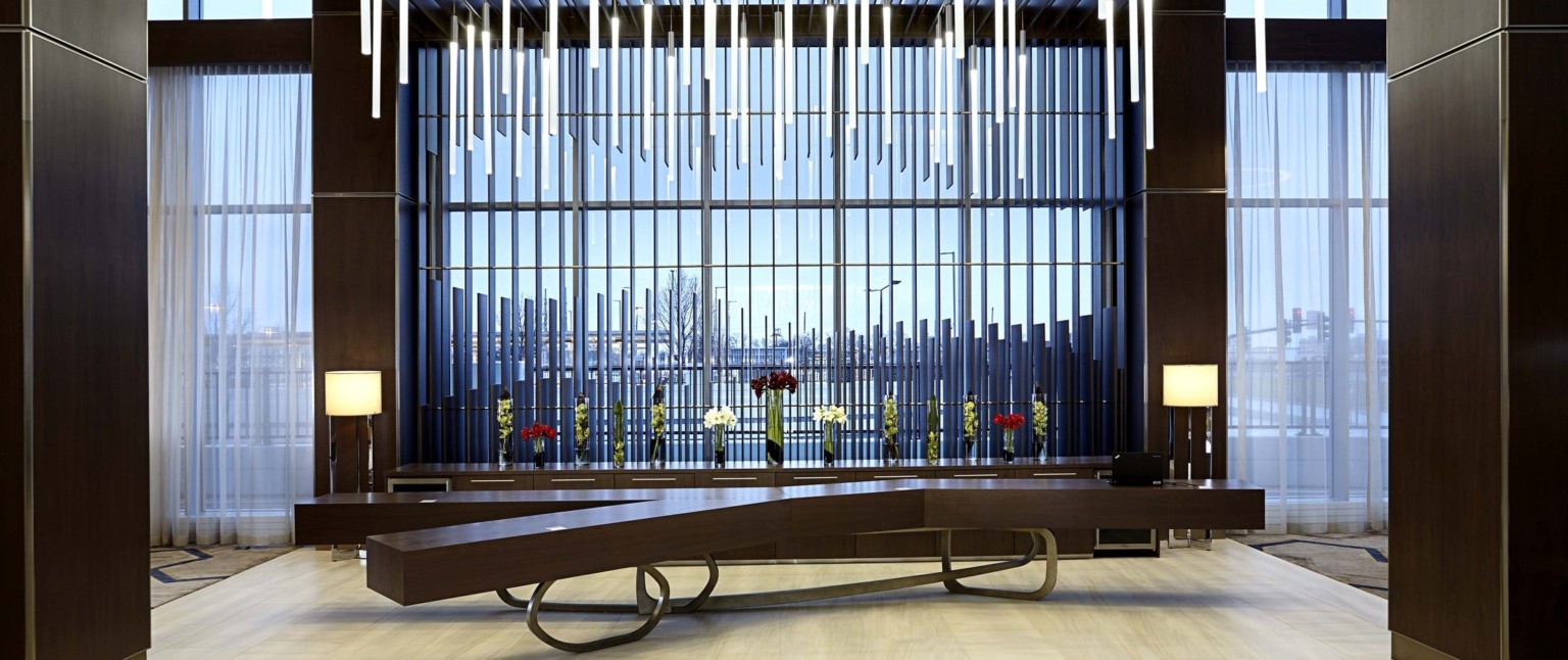 Interior view with wooden Y shaped table in front of matching set of drawers in front of floor to ceiling windows