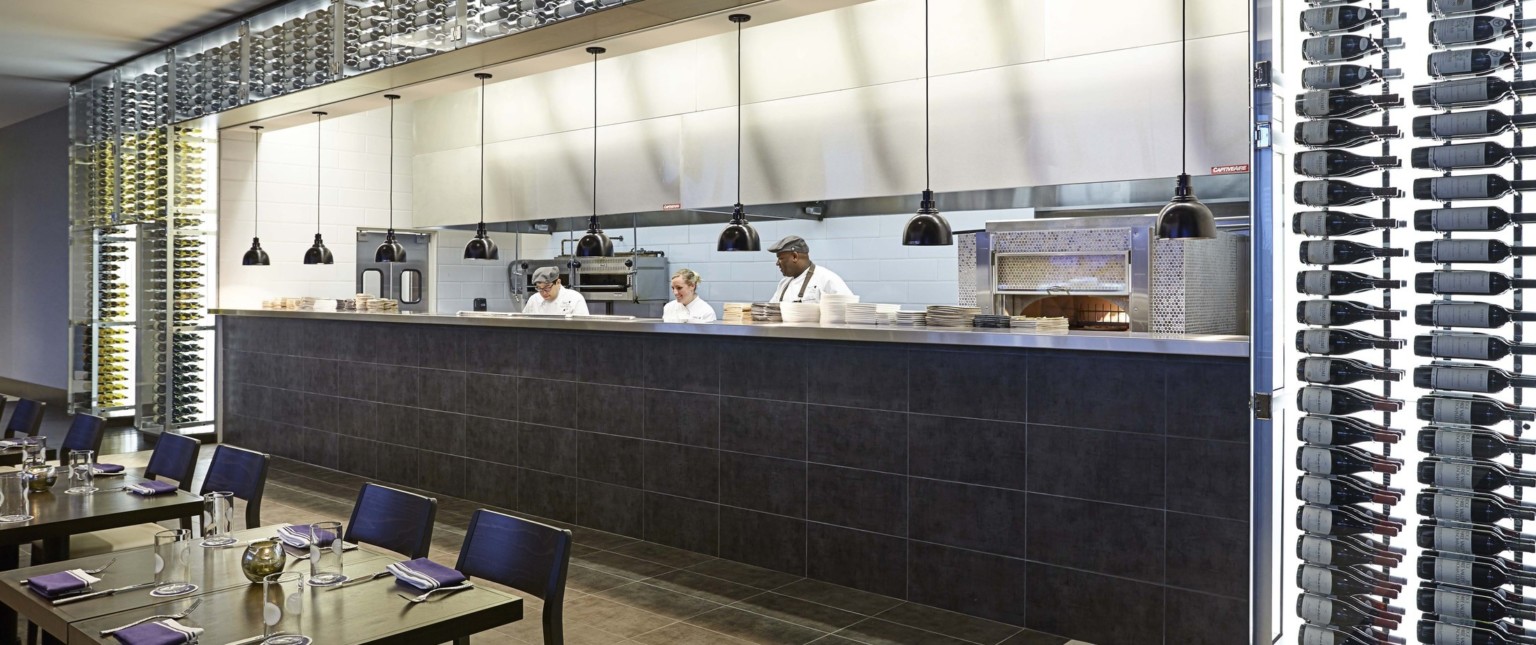 Open kitchen layout with dark tiled counter and black pendant lamps adjoining dining area with dark wood chairs and tables