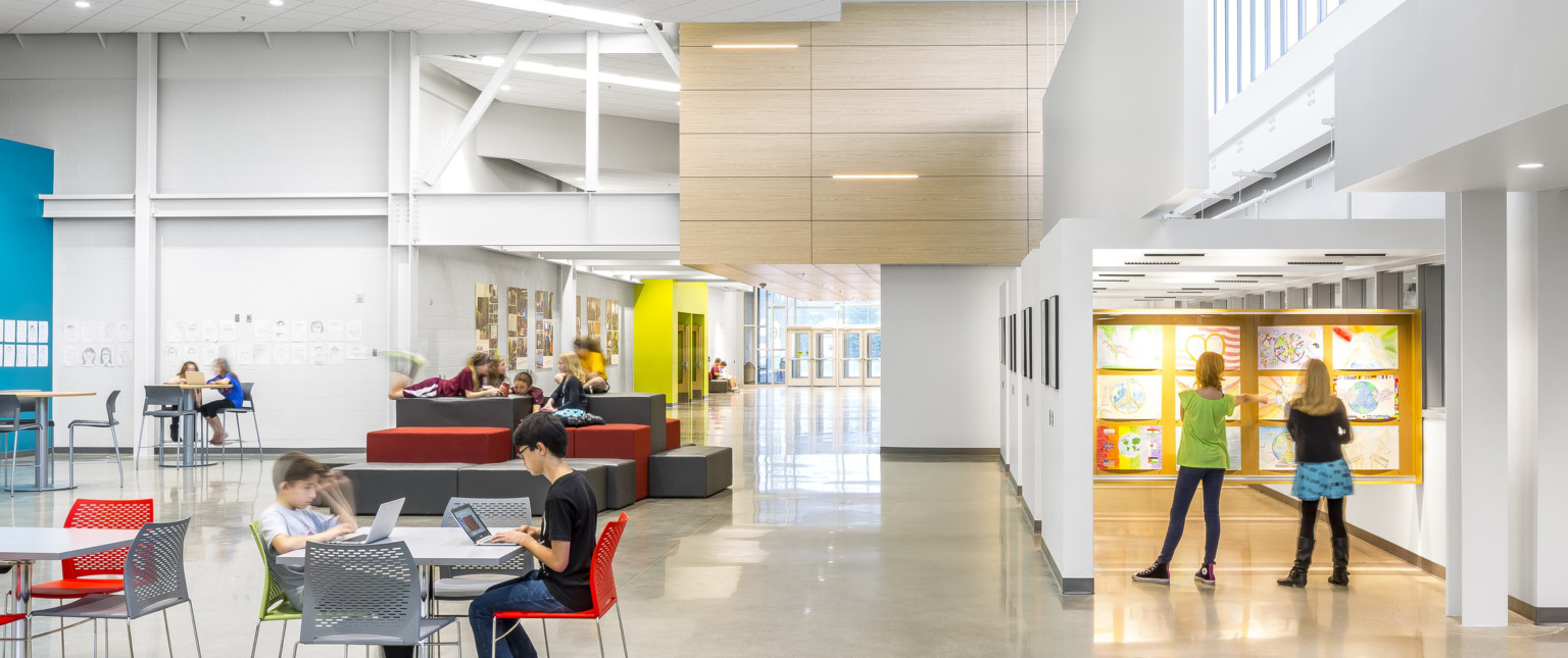 A white room with exposed structural beams. Ergonomic seating. Right, an atrium with art displayed. Wood drop ceiling detail