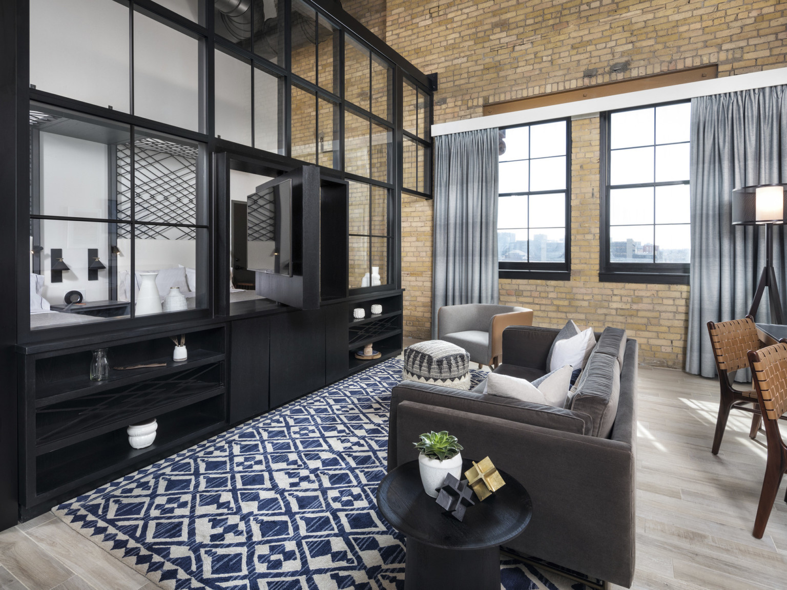 interior design for a luxury hotel room at the Canopy by Hilton Minneapolis Mill District, blue triangle rug fills the space, large metal black built-in separates the living room from the bedroom, adaptive reuse hotel