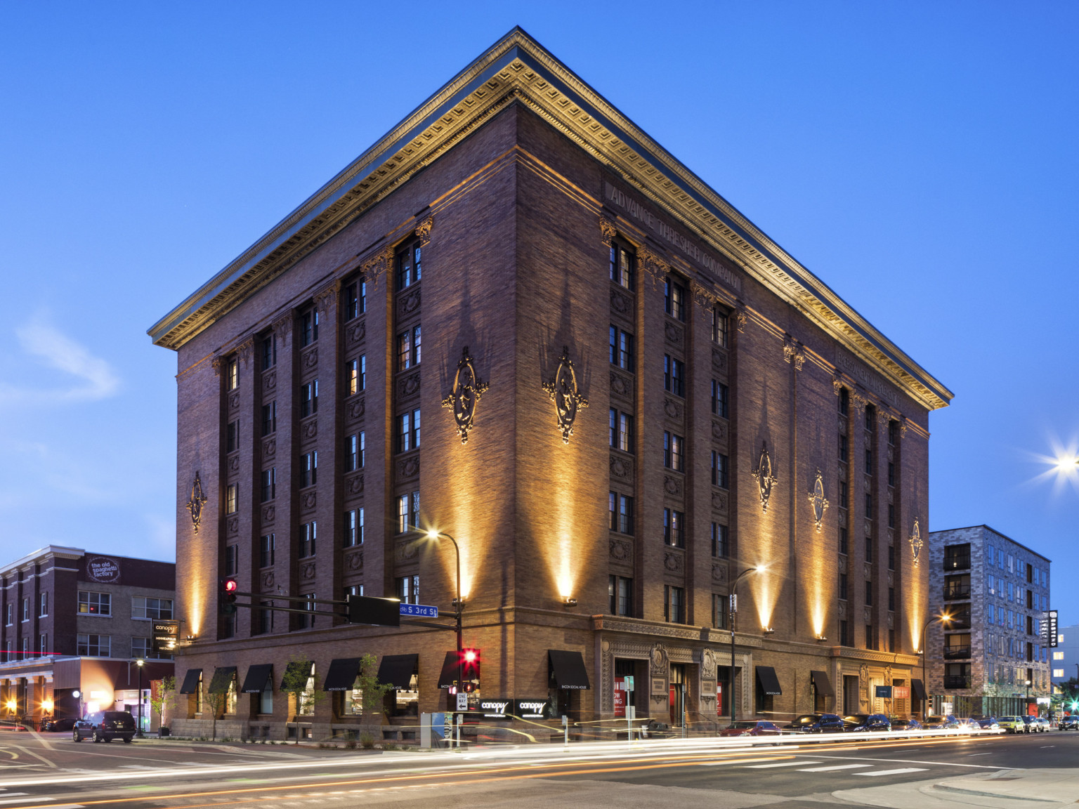 6 story brick building seen from corner across intersection. Carved details at roof and along walls are light from below, adaptive reuse hotel