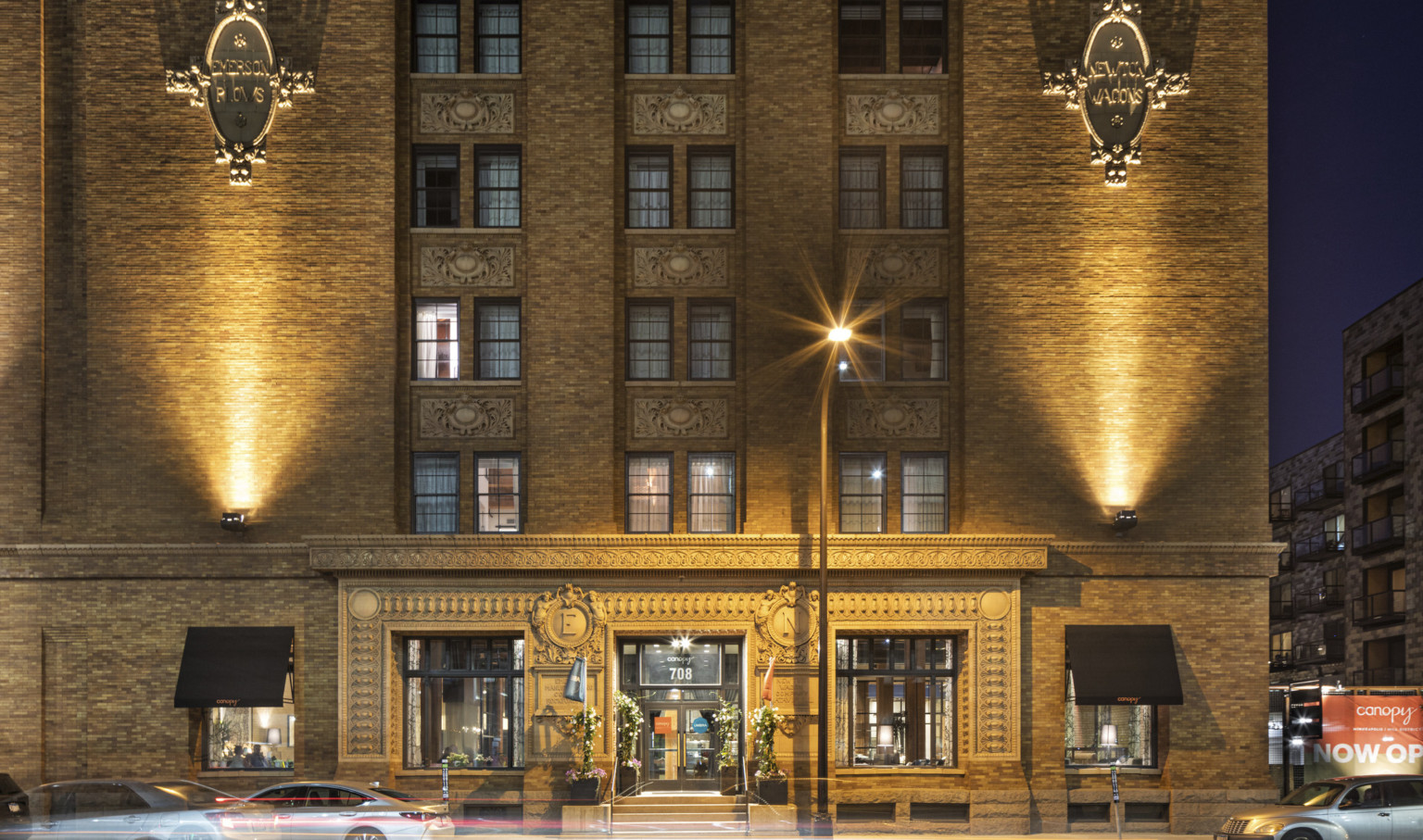 Exterior view of historic mill district cement building with uplighting and ornamental emblems at the Canopy Mill District