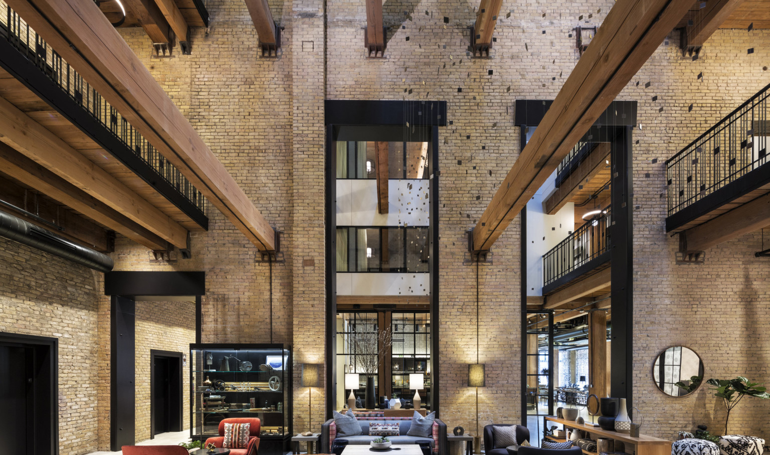 Interior atrium with exposed brick. Seating area at center and wood beams overhead. 2 walkways on sides above with metal rail